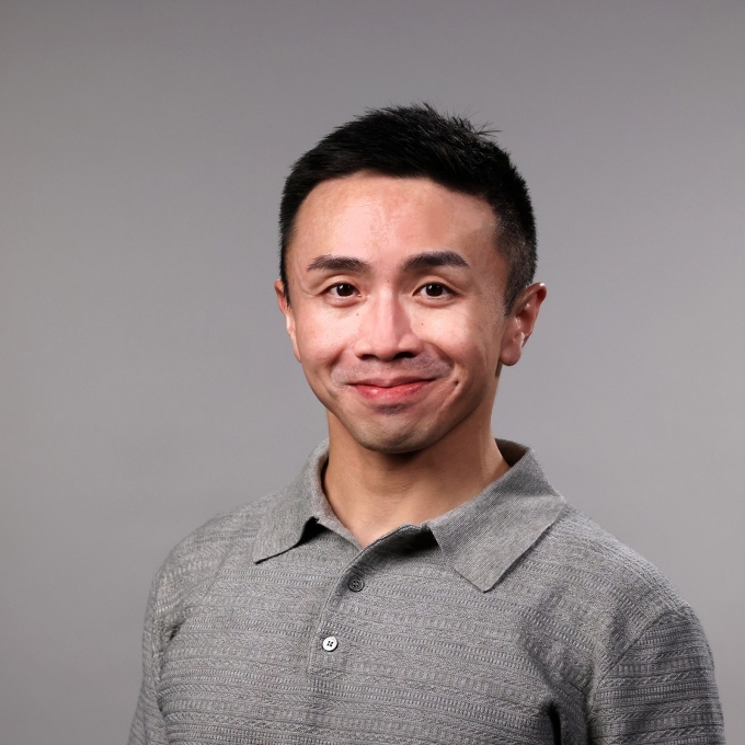a man with short dark hair wearing a grey collared shirt on a grey background