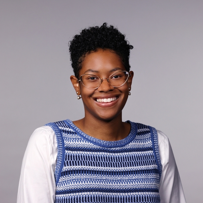 Woman with a blue striped vest, white shirt, glasses, and short hair