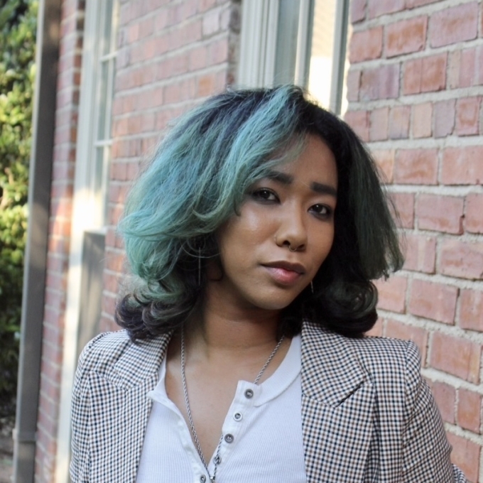 a professional wearing a grey blazer with dark hair smiling in front of a brick building