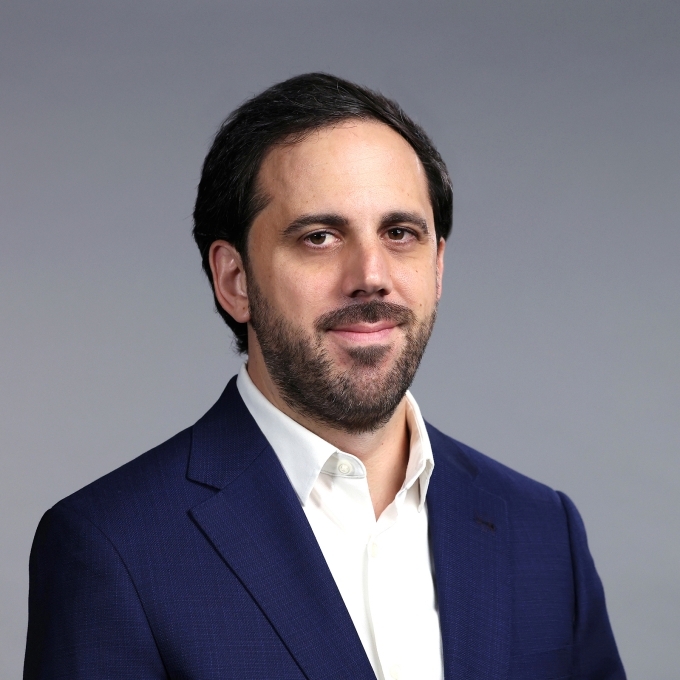 a man with facial hair and short brown hair wearing a collared white shirt and blue blazer