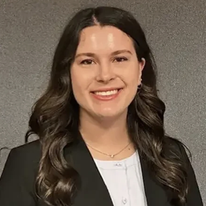 a young woman with long curly dark hair wearing a black blazer and white blouse
