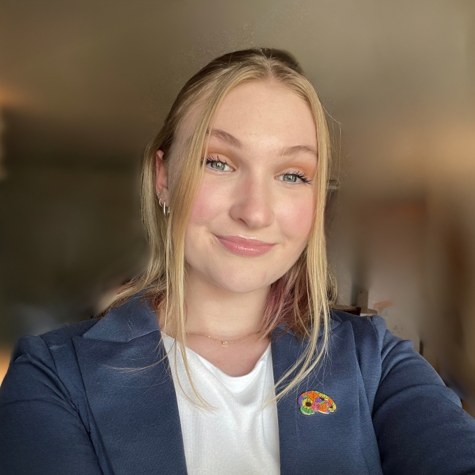 Blonde woman, likely in her 20s, takes a selfie in a blue blazer and white blouse
