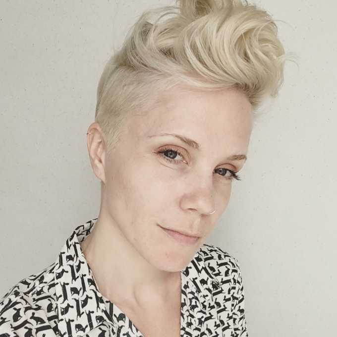 A person with platinum blonde hair in a pixie cut and a black and white blouse
