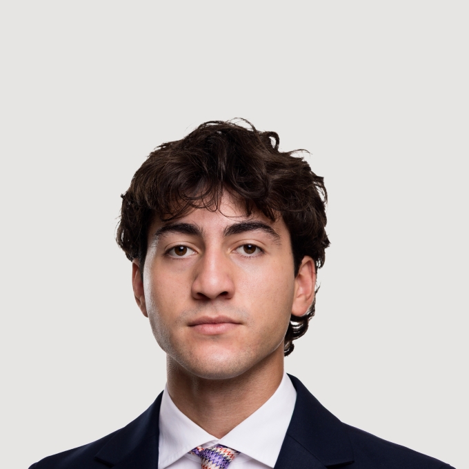 A male student in a suit and pink striped tie with dark curly hair and a neutral expression
