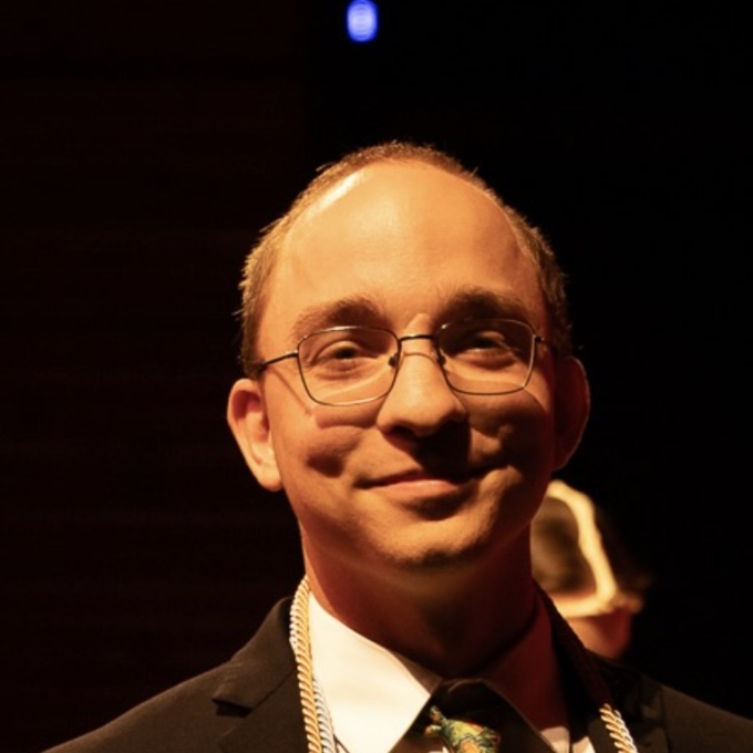 A man with short dark hair, round glasses, and a suit and tie