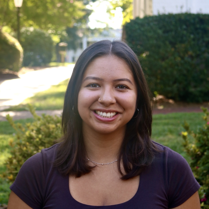 Alex smiling outdoors in a dark scoop-neck top with shoulder-length dark hair