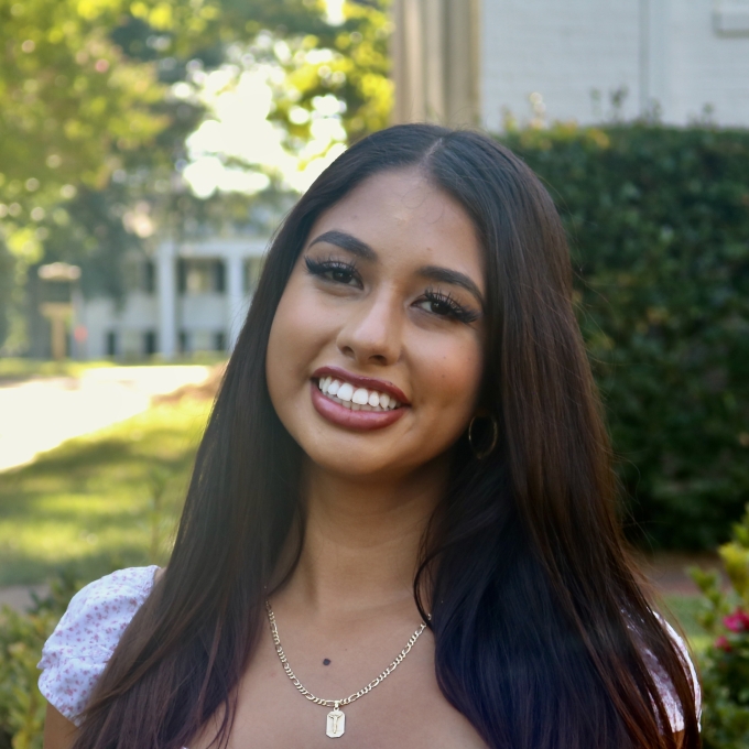 Priscila smiling outdoors with long dark hair wearing a floral print top
