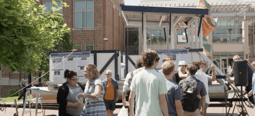 a group of students stand in front of a solar-powered boat on a sunny day