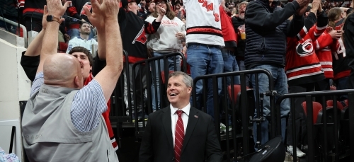 an older white man smiles at hockey fans cheering