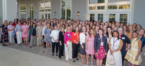 A group of ~100 colorfully-dressed women on a patio at the beach