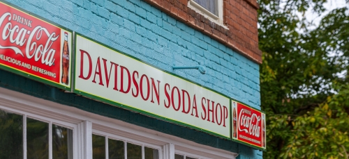 A "Davidson Soda Shop" sign flanked by two Coca-Cola logos on a blue brick storefront