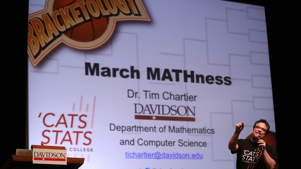 Tim Chartier stands on stage by presentation and talks to audience