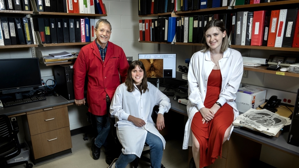 Two students and a professor stand around a lab together smiling