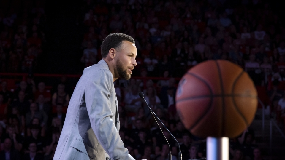 a man in a grey suit speaks into a microphone on a stage
