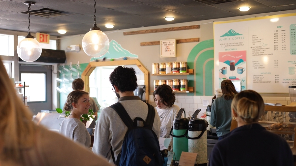 a group of students smile and talk while waiting in line at a coffee shop