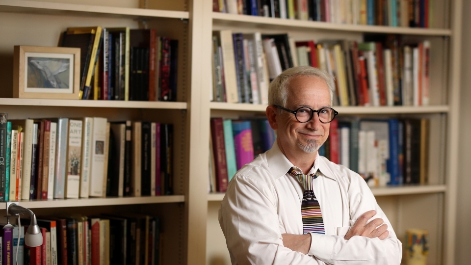 a middle aged white man standing in front of a bookcase smiling