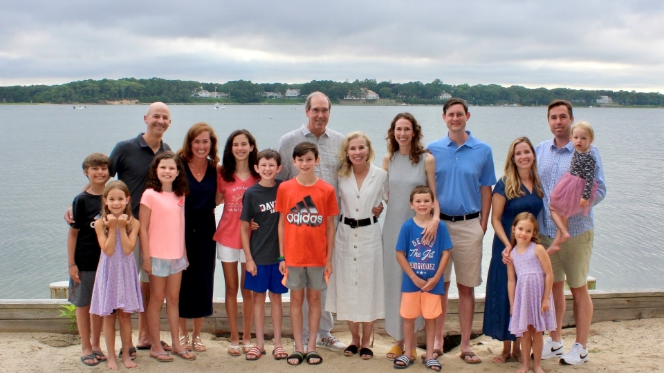 a white family standing in front of a lake on a sandy patch of land