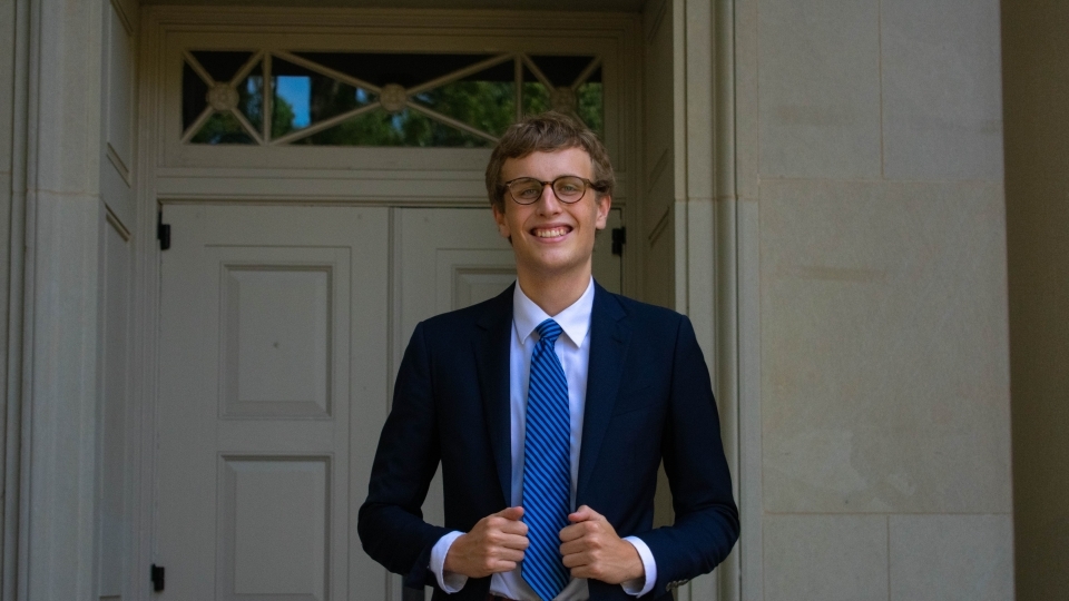 a young white man wearing a suit and tie standing in front of an old building