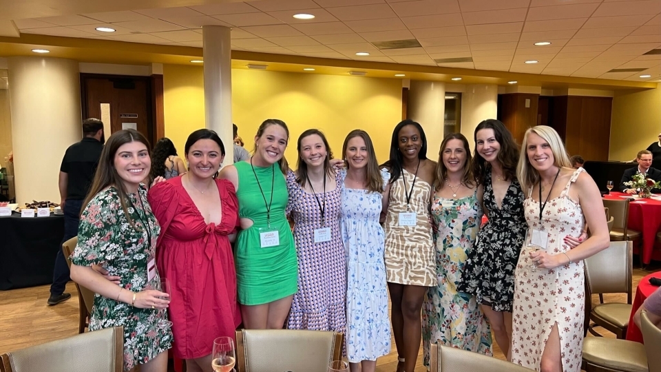 a group of young women in dresses and nametags smile standing together