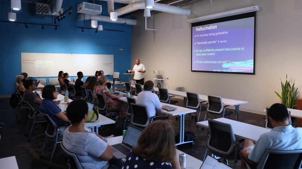 a modern classroom where adults sit around on laptops listening to a speaker