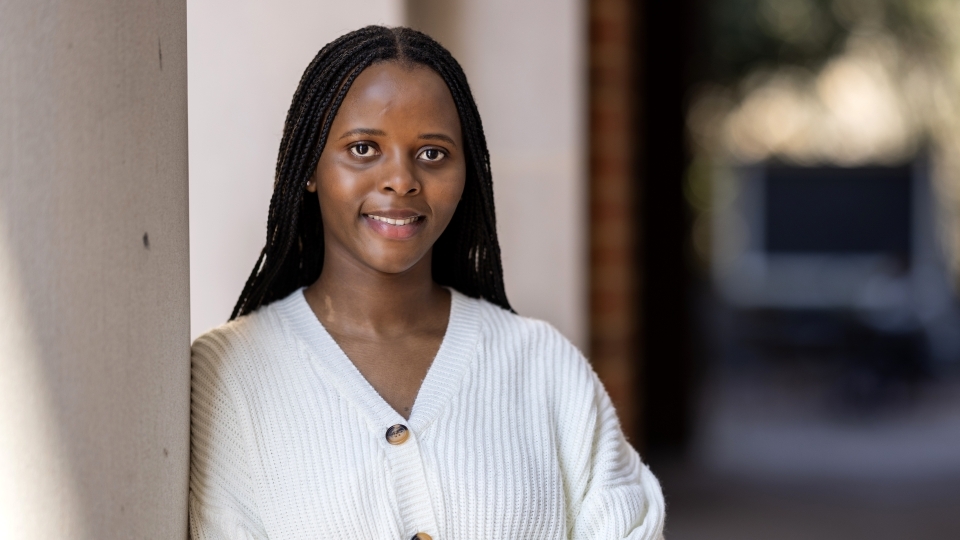 a young Black woman wearing a white sweater leaning against a column