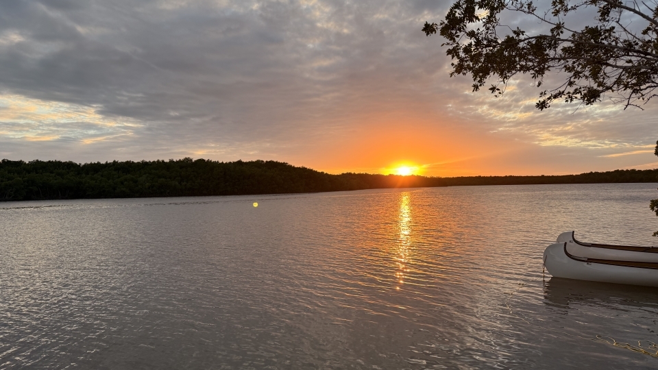 a body of water at sunset with a canoe in the foreground