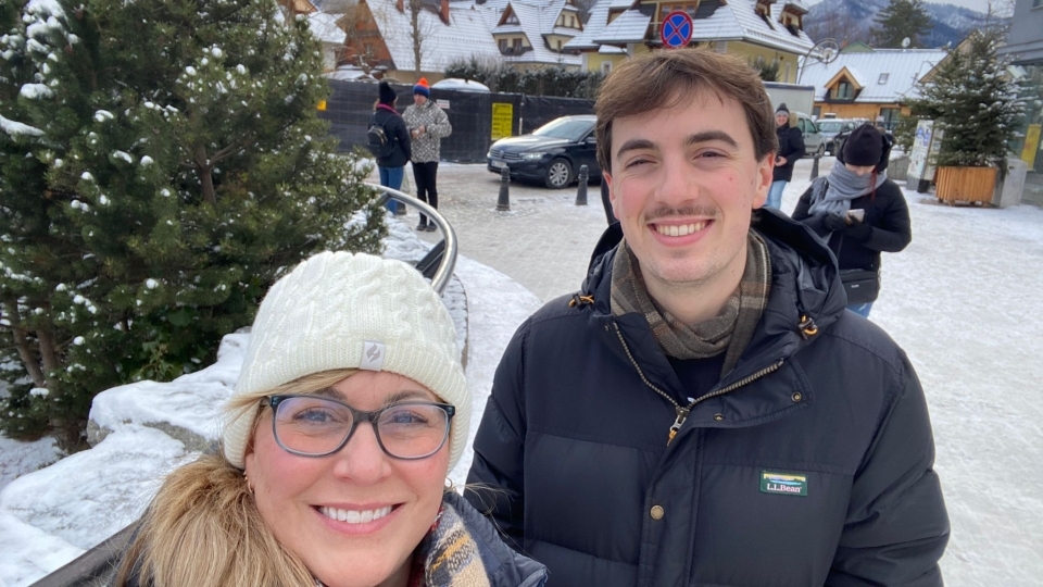 an older white woman and a younger white man smile in front of a snowy landscape