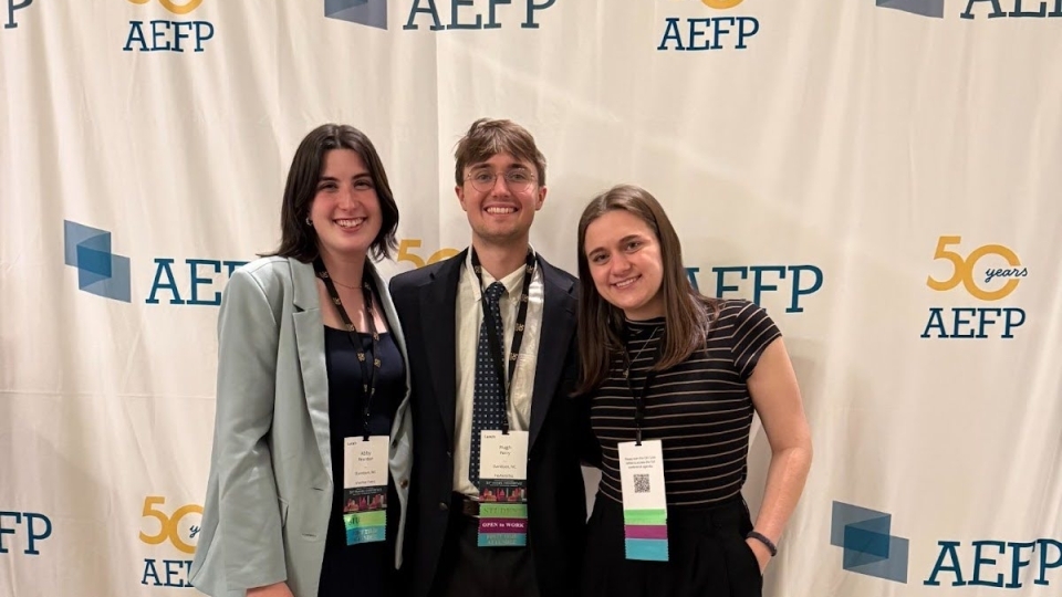 a group of three students in business casual smile together at a conference