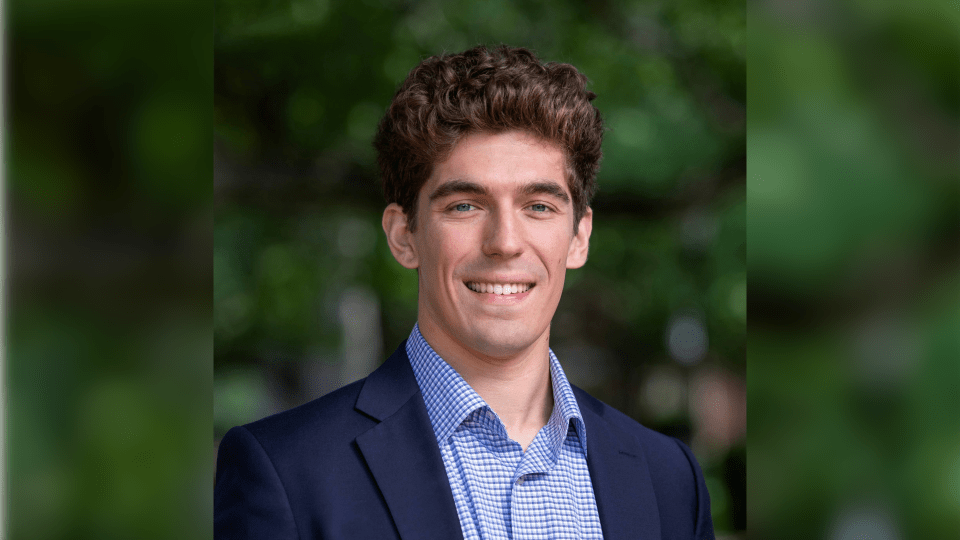 a young white man wearing a collared shirt and jacket with curly brown hair