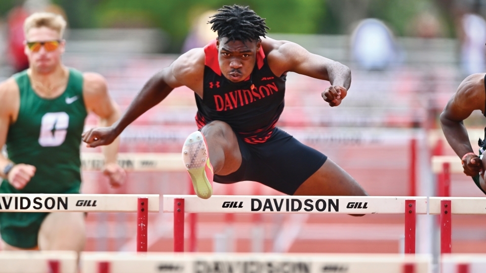 a young Black man hurdles on a track wearing a Davidson College uniform