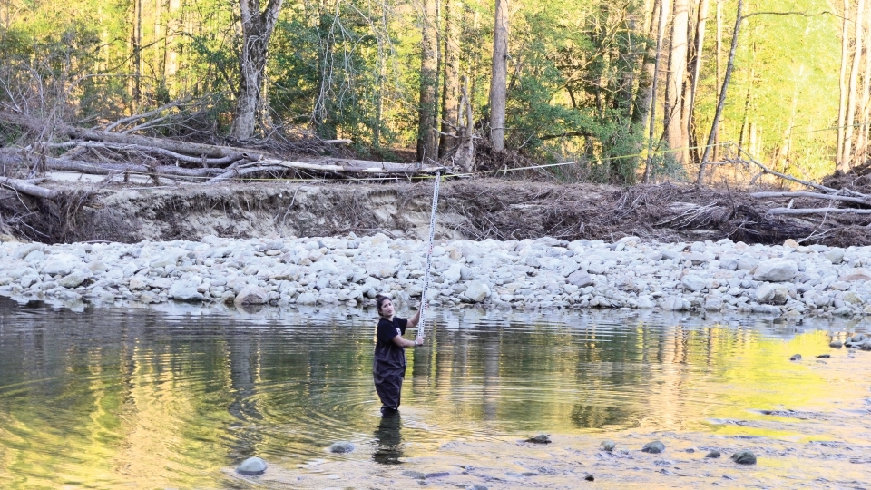 a young woman measures water in a forested area on a sunny day