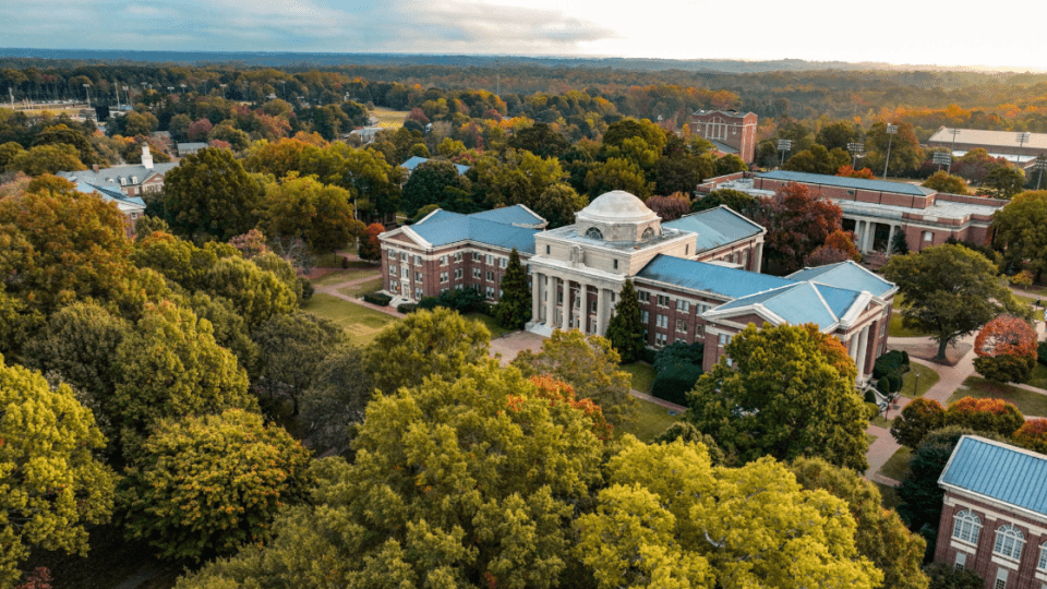 an aerial view of a college campus with brick buildings, green trees and a lake in the distance