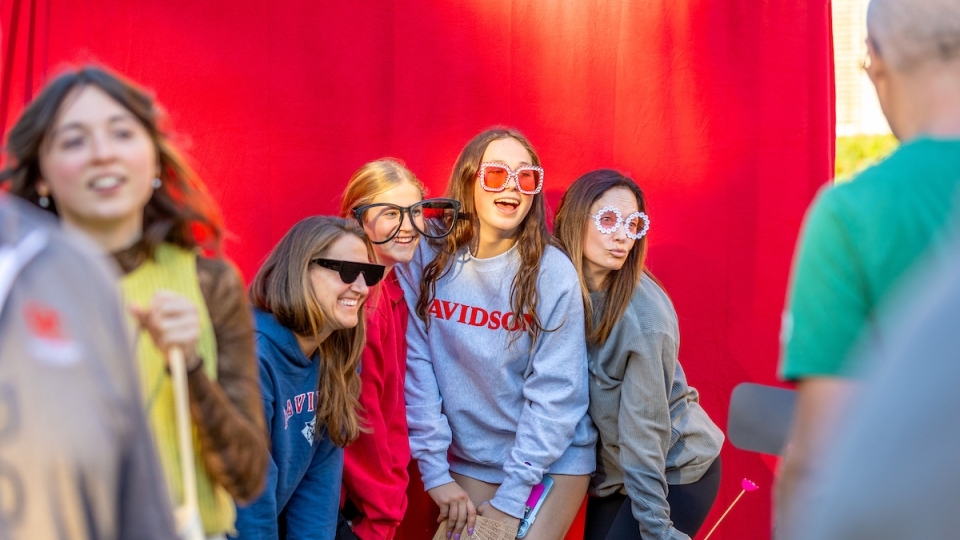 a group of young women and their moms pose in front of a red photo booth