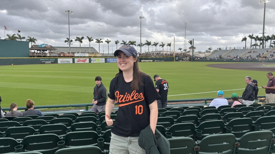 a young woman wearing an Orioles baseball jersey and hat in front of a baseball stadium