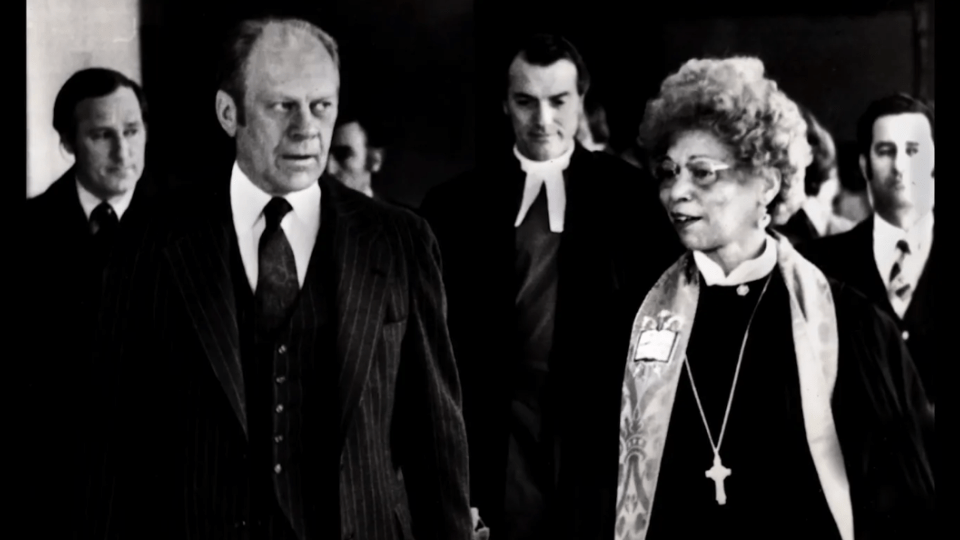 a Black woman walks and talks with an older white man in a black and white photograph
