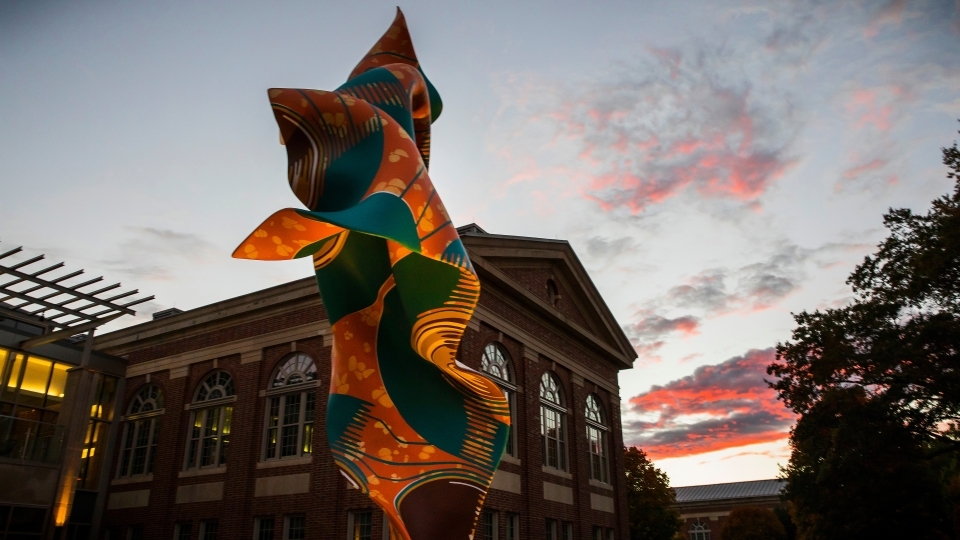 a colorful sculpture in front of an academic building at sunset