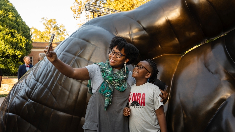 two young people smile and take a selfie in front of a sculpture