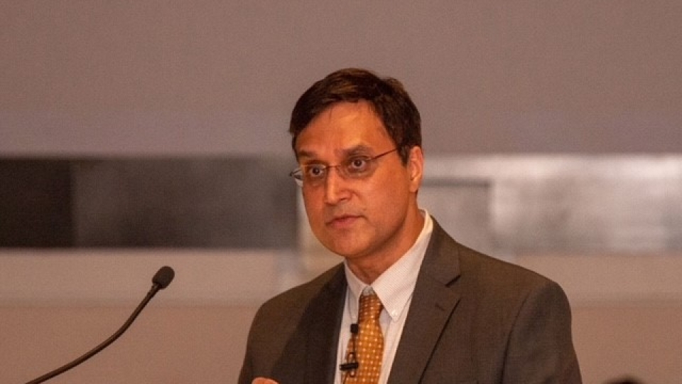 a man wearing a suit and tie speaks into a microphone on stage