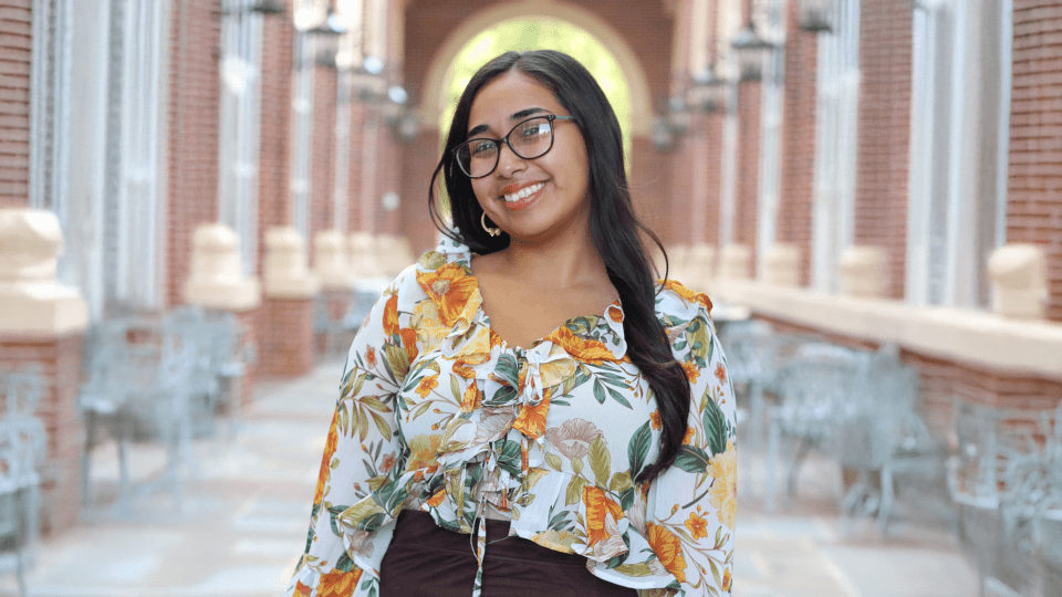 Headshot of young female student on campus, with long dark hair and glasses