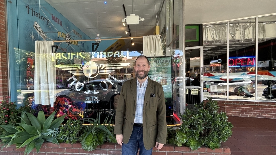 a man stands in front of a pinball museum smiling