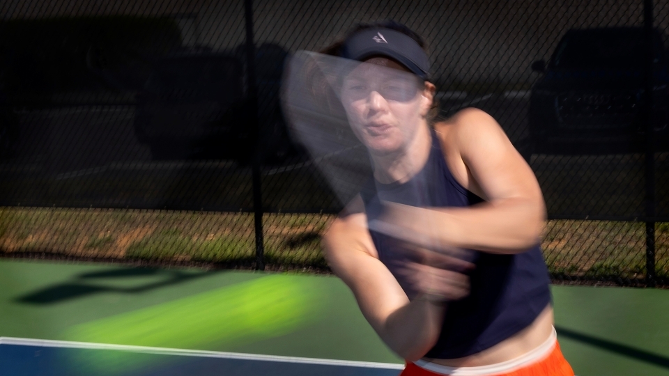 a young woman swings at a pickleball on a court