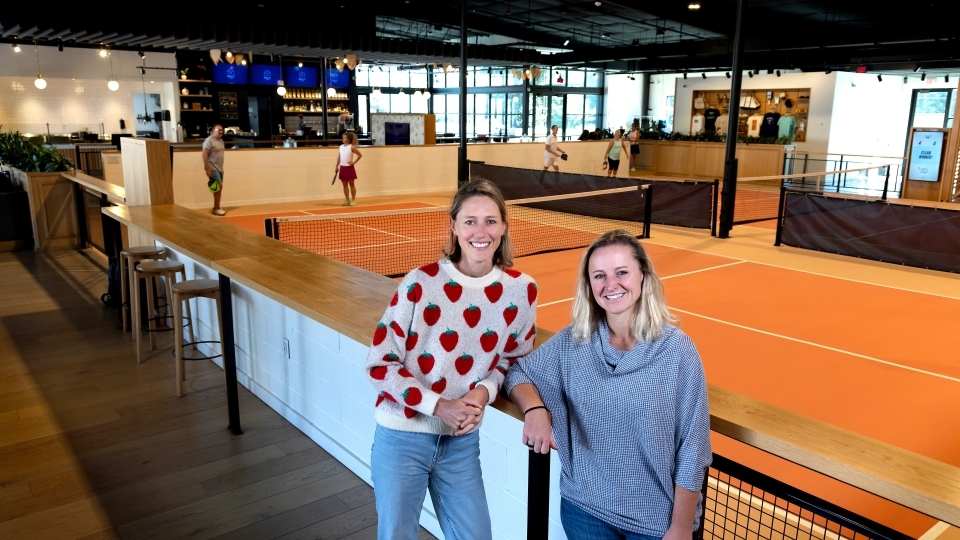two women stand in front of an indoor pickleball space