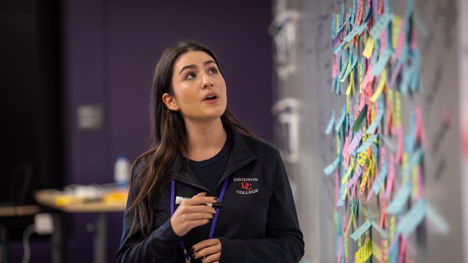 Female student speaks in front of a wall of sticky notes