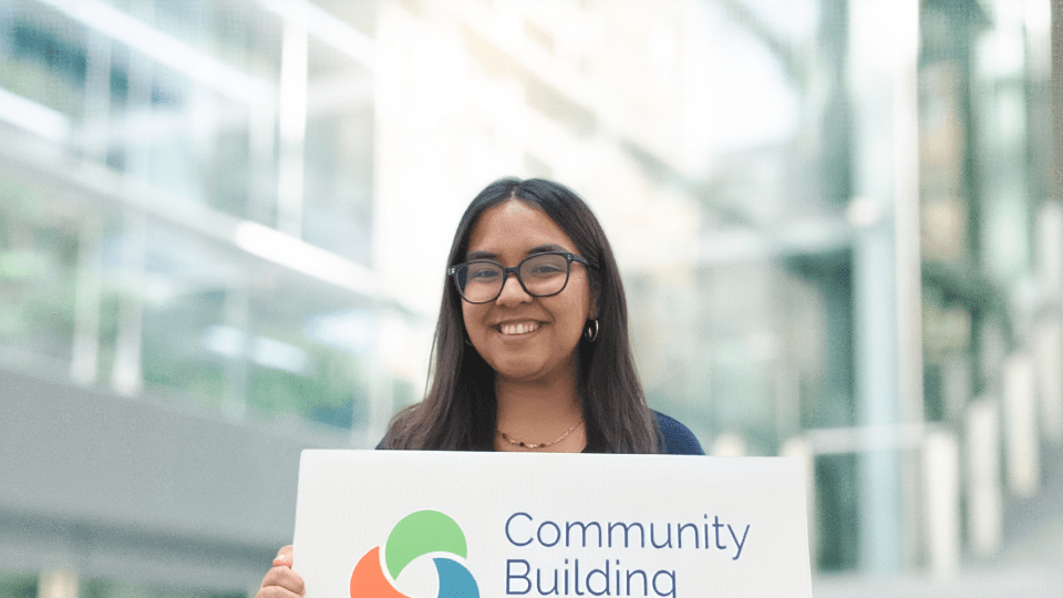 a young woman holds a sign that says "community building initiative"