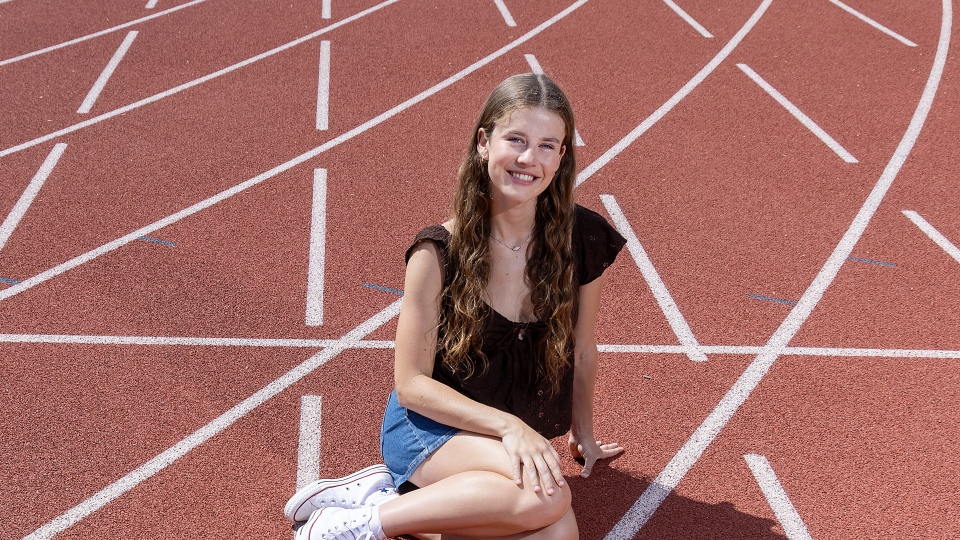 A young woman with long brown hair on a track field