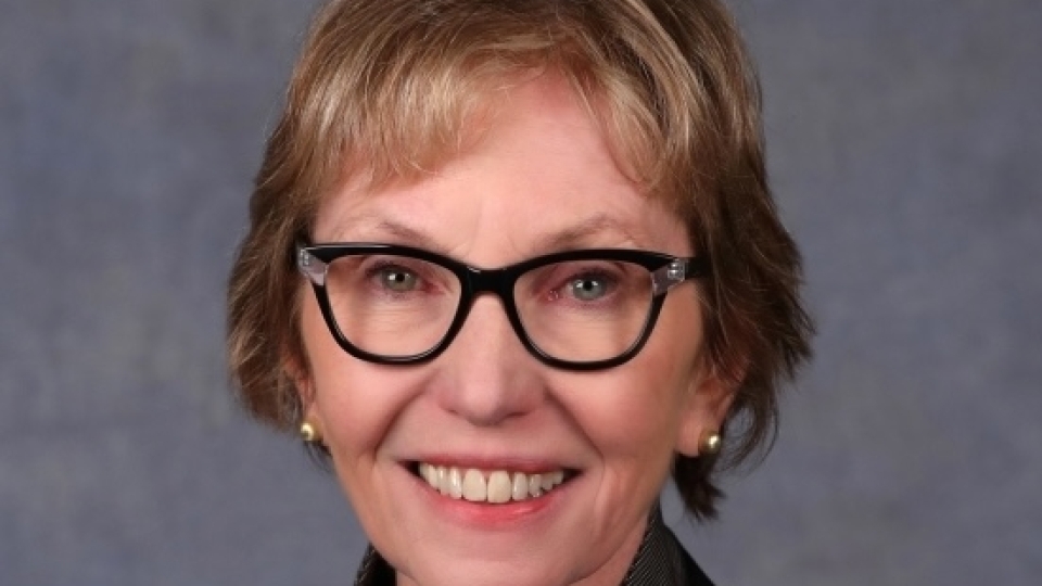 A white woman with blonde short hair and dark rimmed glasses
