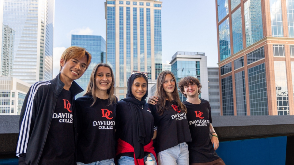 Five students in black and red Davidosn College shirts, with skyscrapers in the background