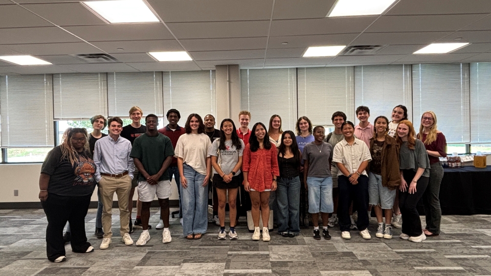 a group of students stand together in an office space smiling