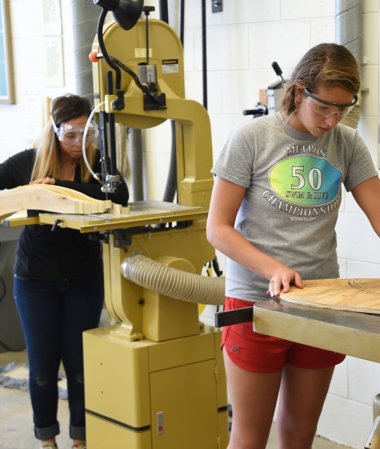Two students work with machinery that cuts wood for a sculpture at the Sculpture Lab