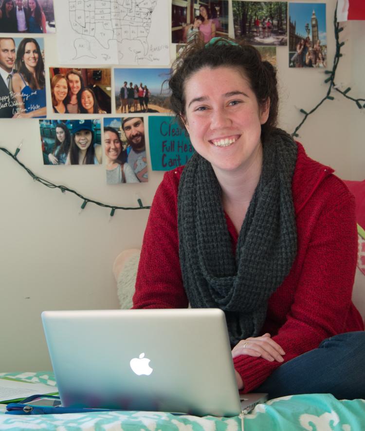 Student sits on her bed in dorm while on laptop